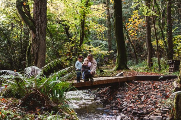 A family crossing a wooden bridge over a stream in autumn woods at Wooda Farm, present in the moment rather than on their phones