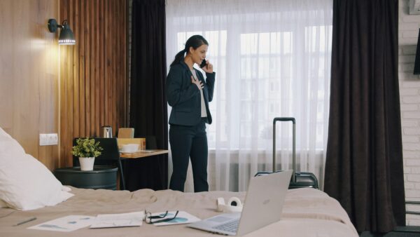 A woman in a dark suit talking on a phone in a hotel room (photo by Vitaly Gariev on Unsplash)