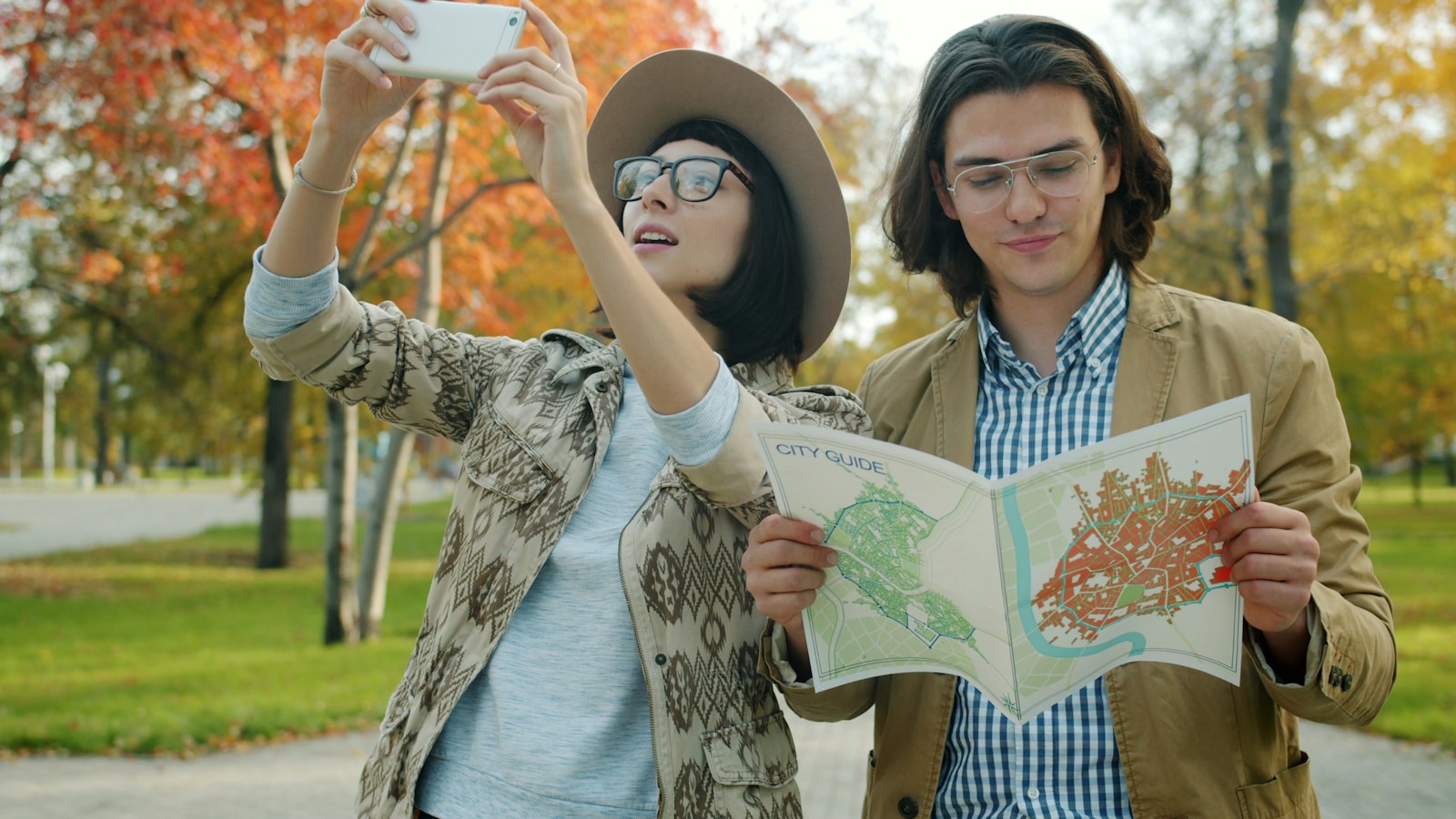 Couple laughing as they look at a map and take a selfie on an autumn day