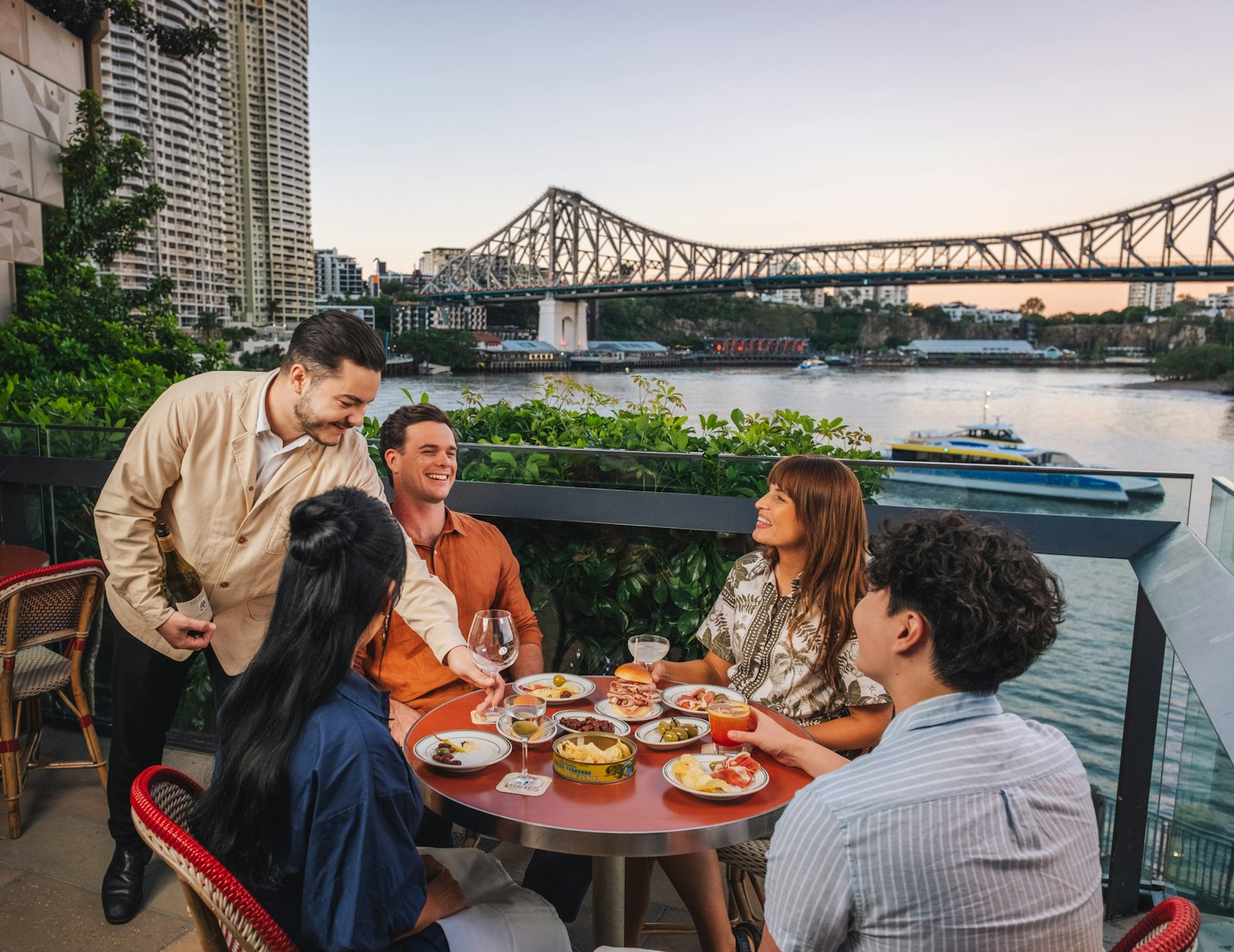 A waiter pouring wine for a group dining on a riverside terrace