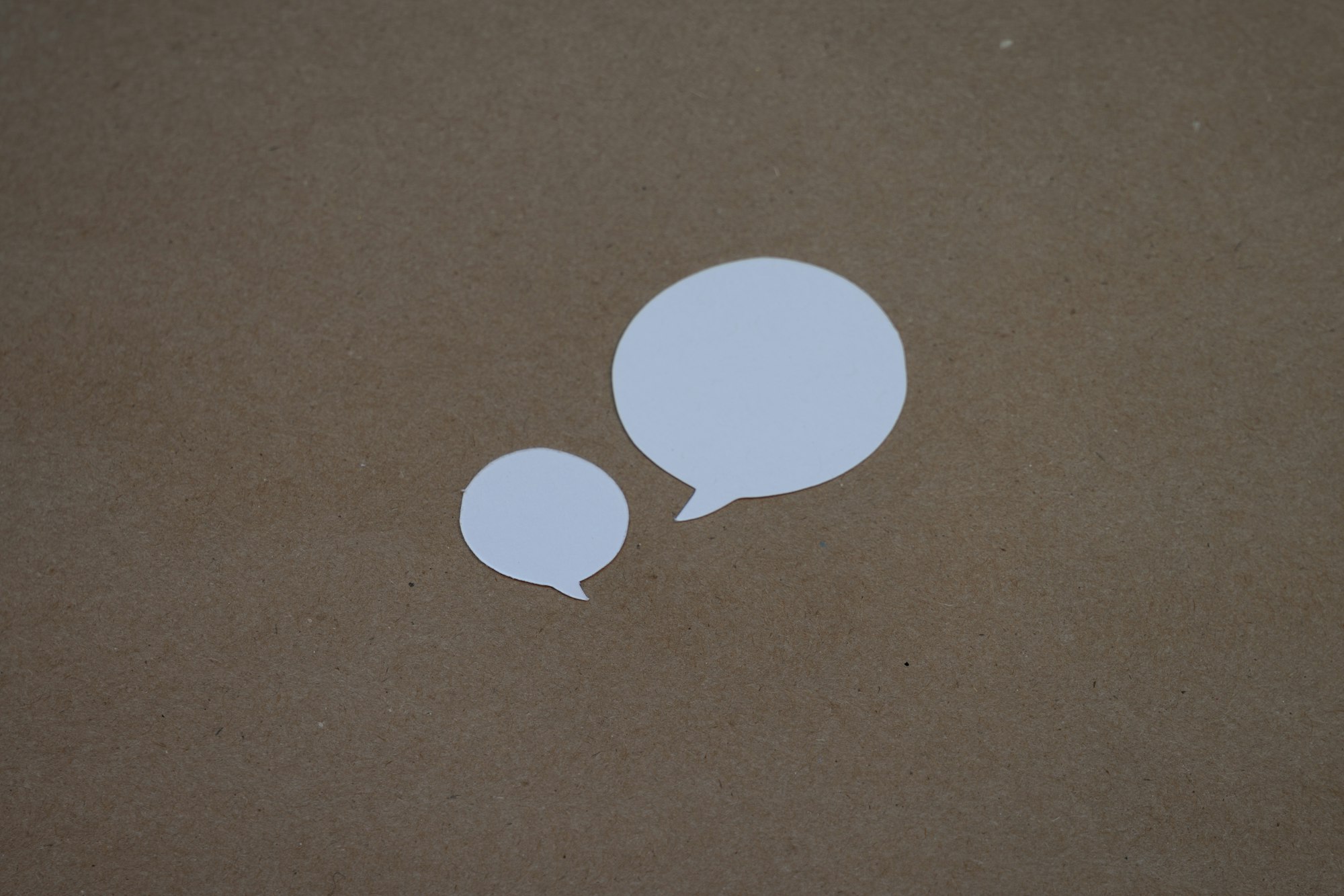 Two white speech bubbles on a brown surface. Photo by Kelly Sikkema on Unsplash.
